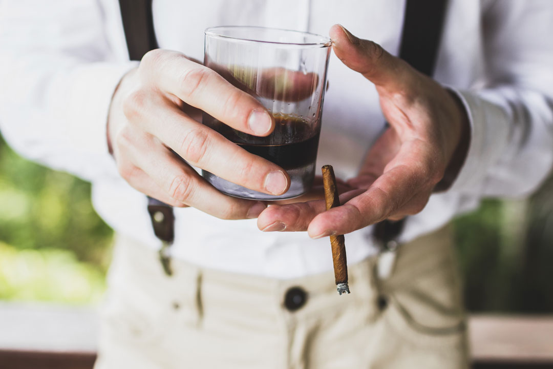 Man drinking whiskey with a smoking a cigar in his hands.